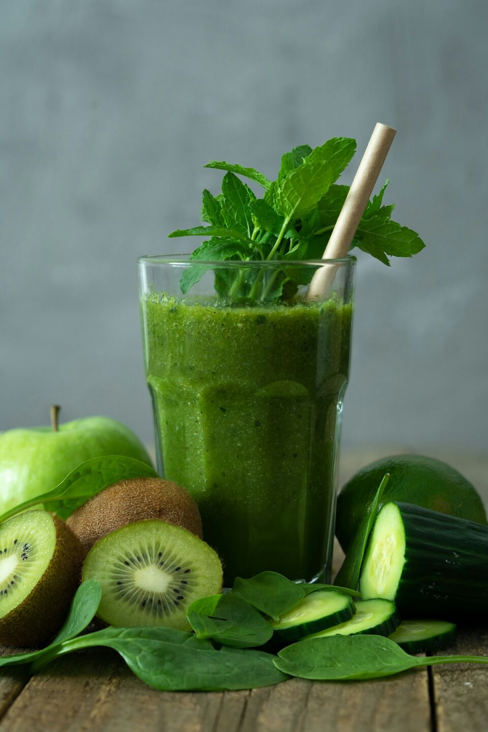 Fresh green smoothie surrounded by leafy greens and fruit